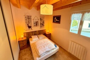 A bedroom with a wooden headboard, a bed with white bedding, two bedside tables with lamps, and a window with a view of greenery. - Apartment with Mezzanine, Mont-Dore (Mont-Dore)