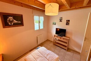 A bedroom with a bed, a television on a wooden stand, a window with curtains, a radiator, and a painting of a dog. - Apartment with Mezzanine, Mont-Dore (Mont-Dore)