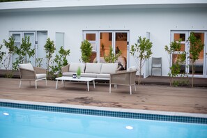 Zona junto a la piscina con sofá, sillas y plantas en macetas.