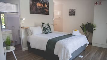 A modern bedroom with a bed, a desk, a mirror, and a door.