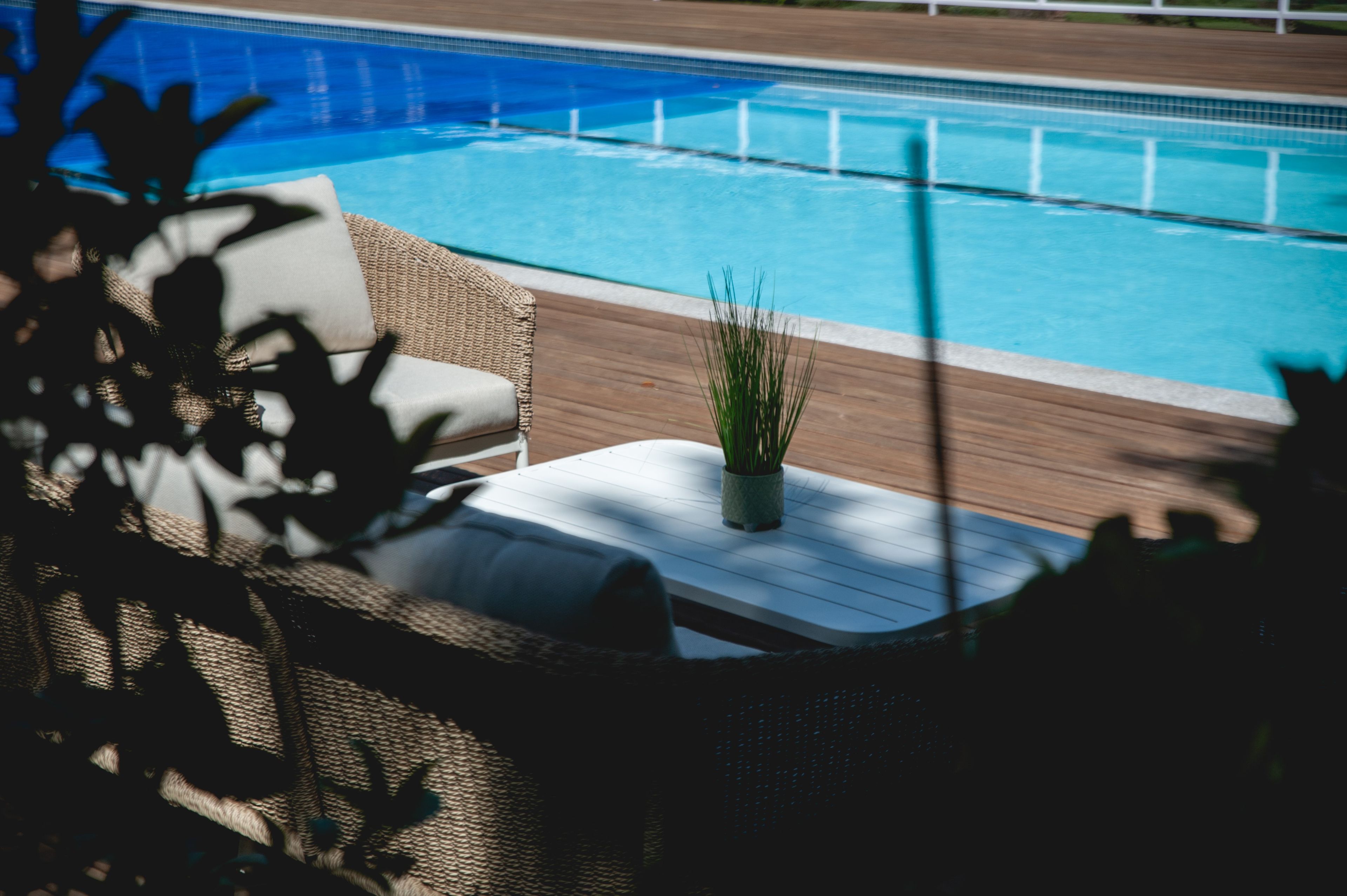 A poolside area with a wicker chair and a small potted plant.