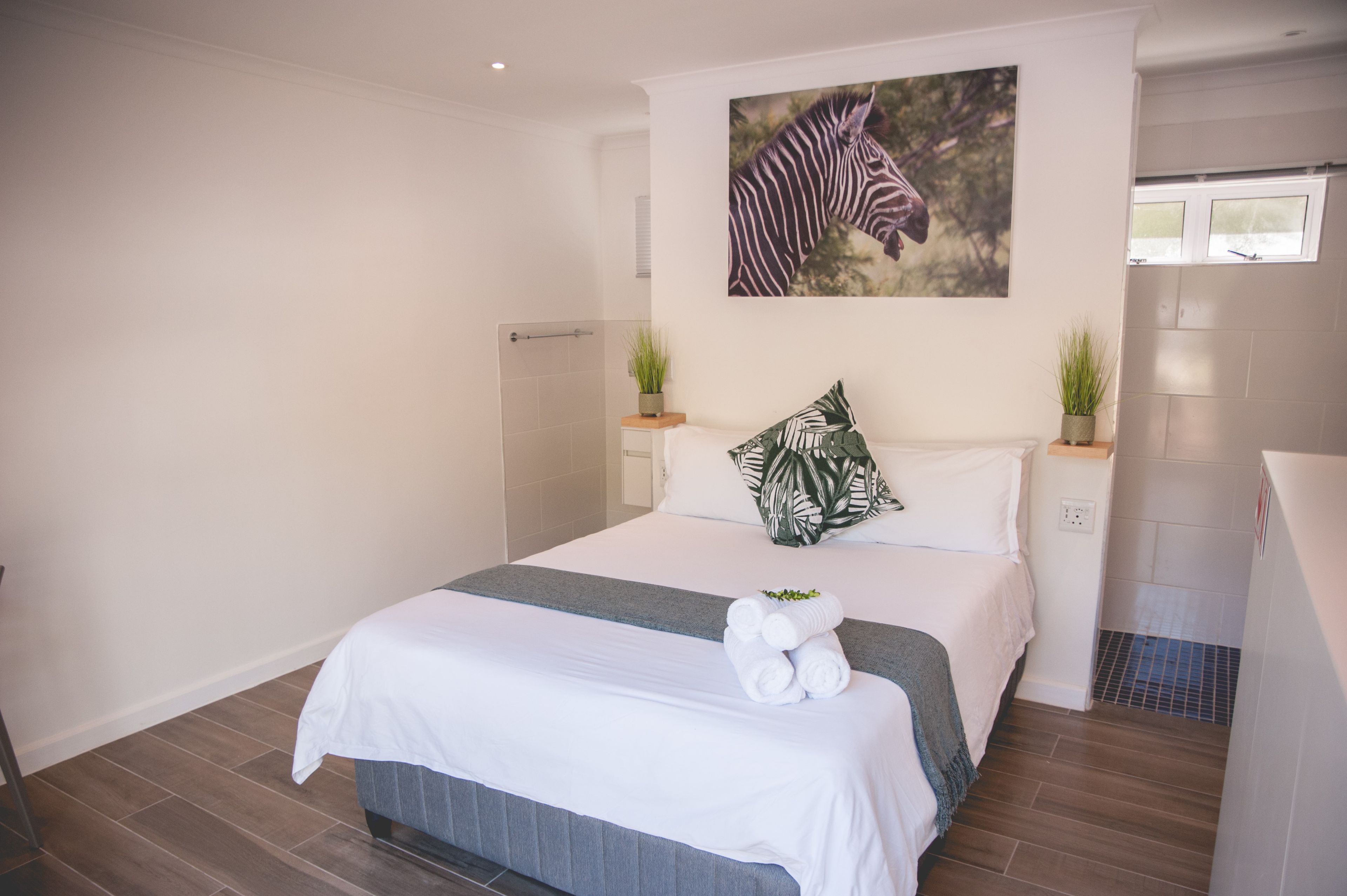 Een hotelkamer met een bed, een schilderij van een zebra, twee potplanten en een douchehoek.