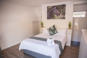 Een hotelkamer met een bed, een schilderij van een zebra, twee potplanten en een douchehoek.