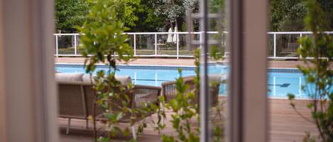 A pool area with a wooden deck, lounge chairs, and a view of the surrounding greenery.