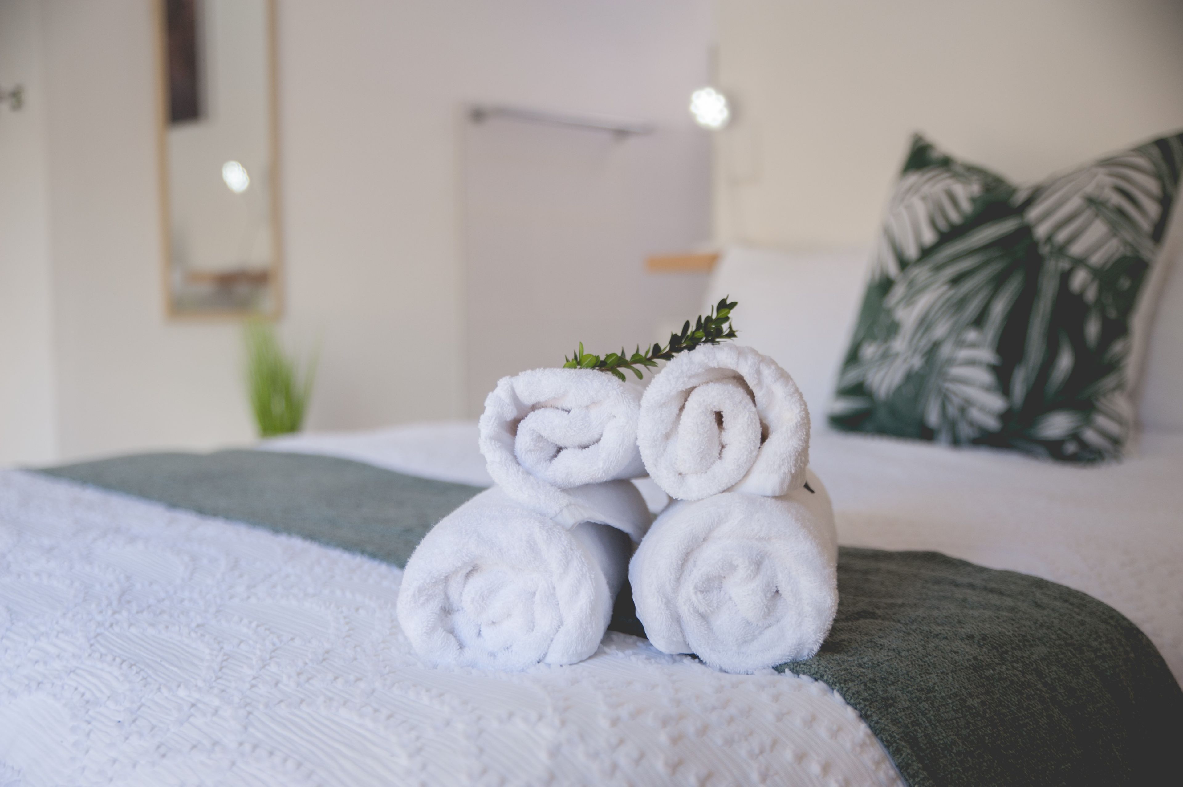 Een net opgemaakt bed met opgerolde witte handdoeken en een groene plaid.