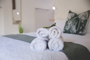 Een net opgemaakt bed met opgerolde witte handdoeken en een groene plaid.