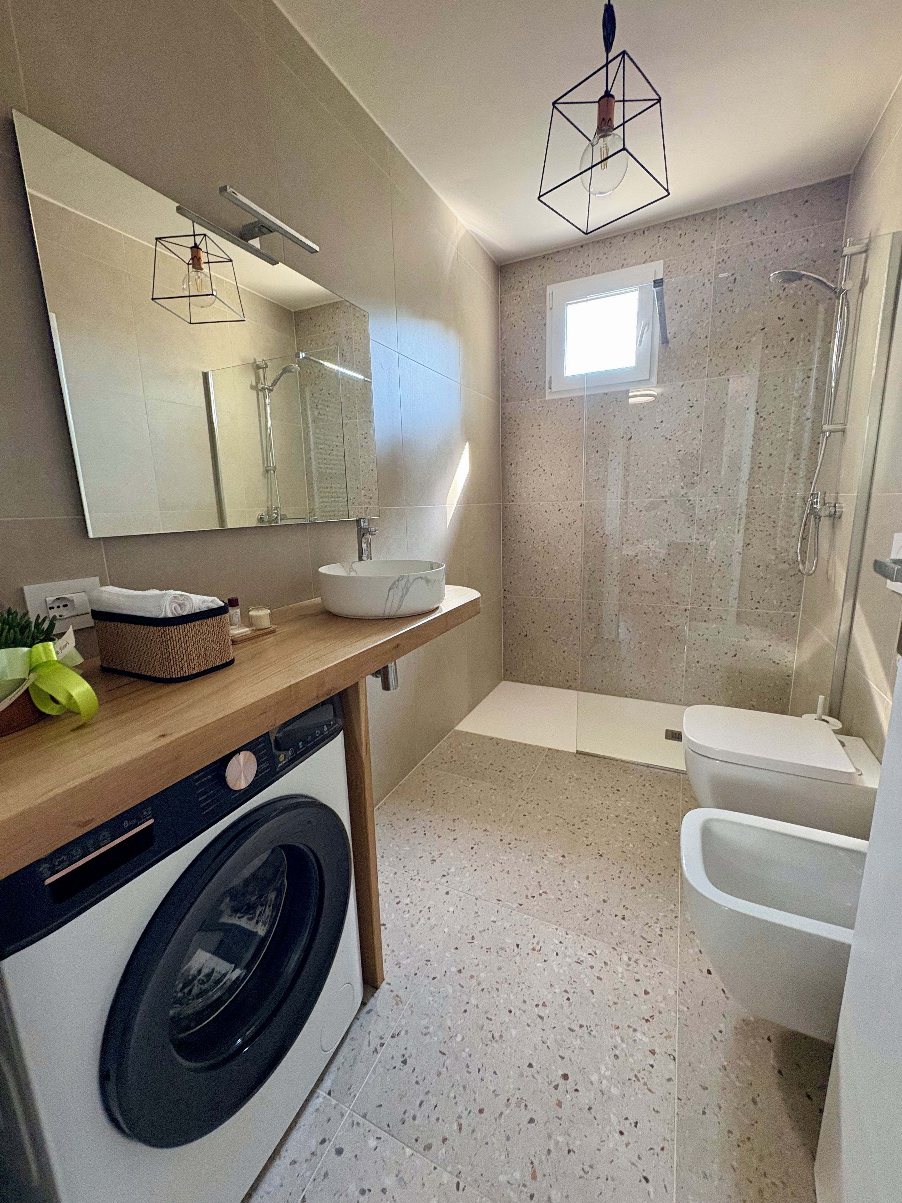 Un bagno moderno con lavatrice, uno specchio grande, una doccia e un water.