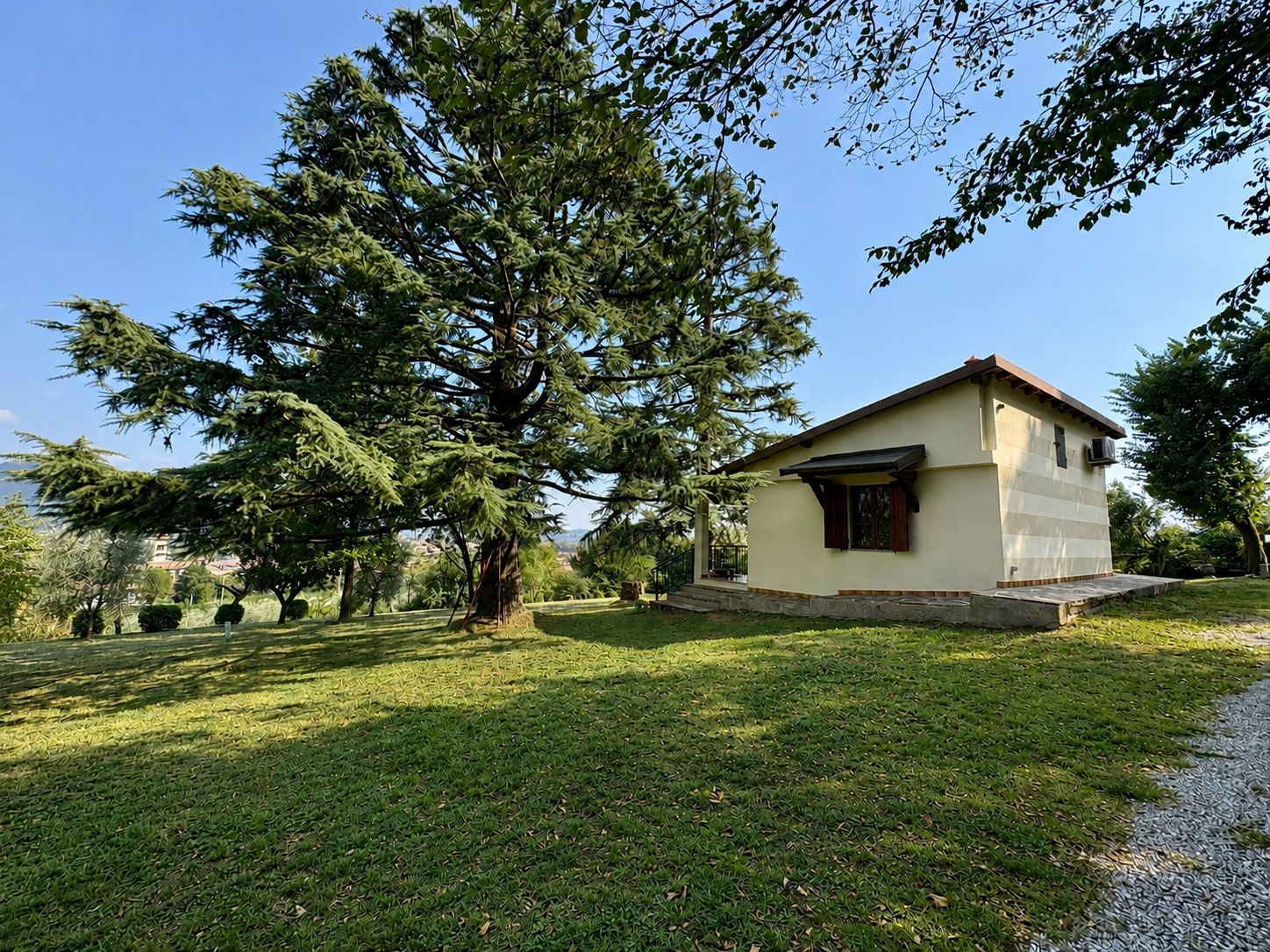 Un piccolo edificio a un piano con tetto spiovente, immerso in un prato curato e alberi di grandi dimensioni.