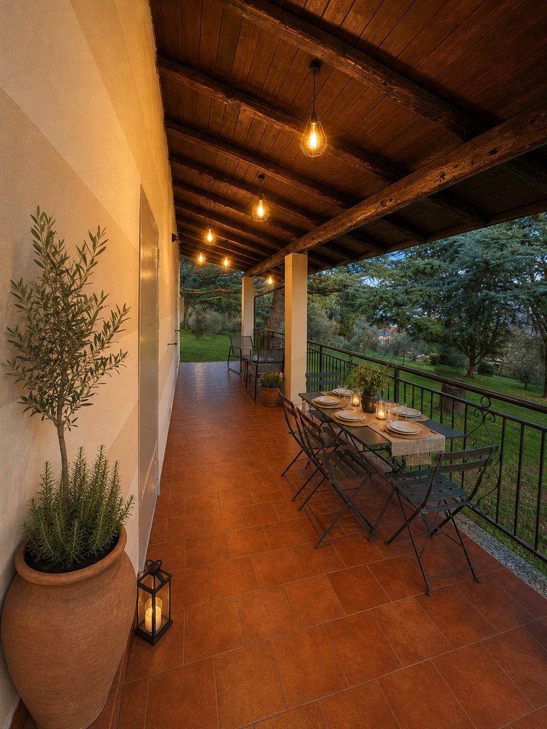 Patio esterno con tavolo apparecchiato per mangiare, circondato da piante in vaso e vista sul giardino.