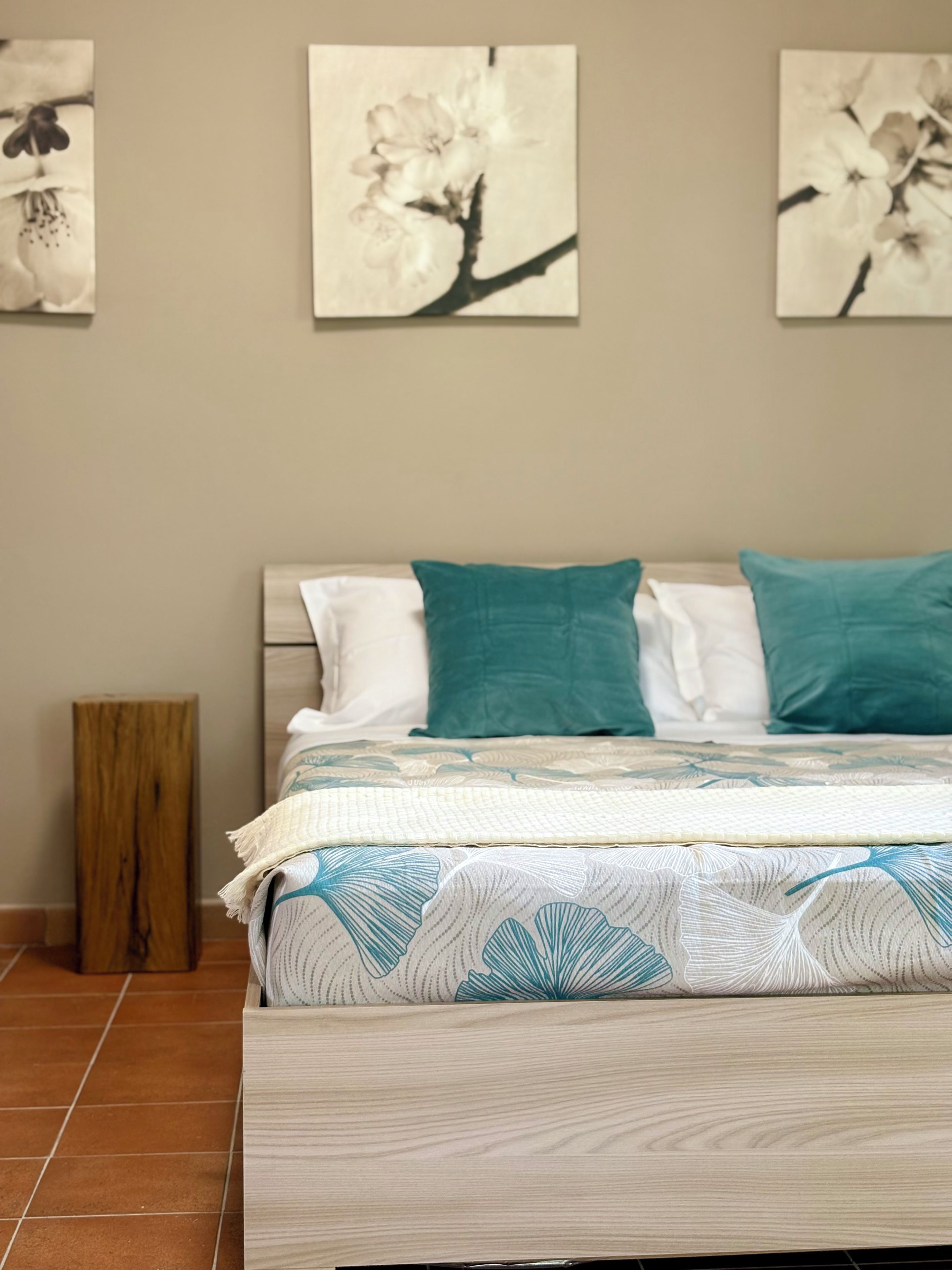 Quarto com cama, almofadas, mesa de cabeceira de madeira e decoração nas paredes.