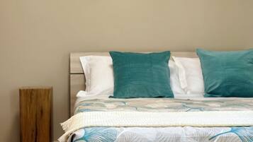 Quarto com cama, almofadas, mesa de cabeceira de madeira e decoração nas paredes.