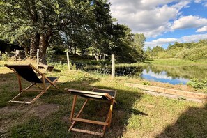 A tranquil outdoor seating area with wooden chairs and a table, surrounded by a natural landscape and a body of water.