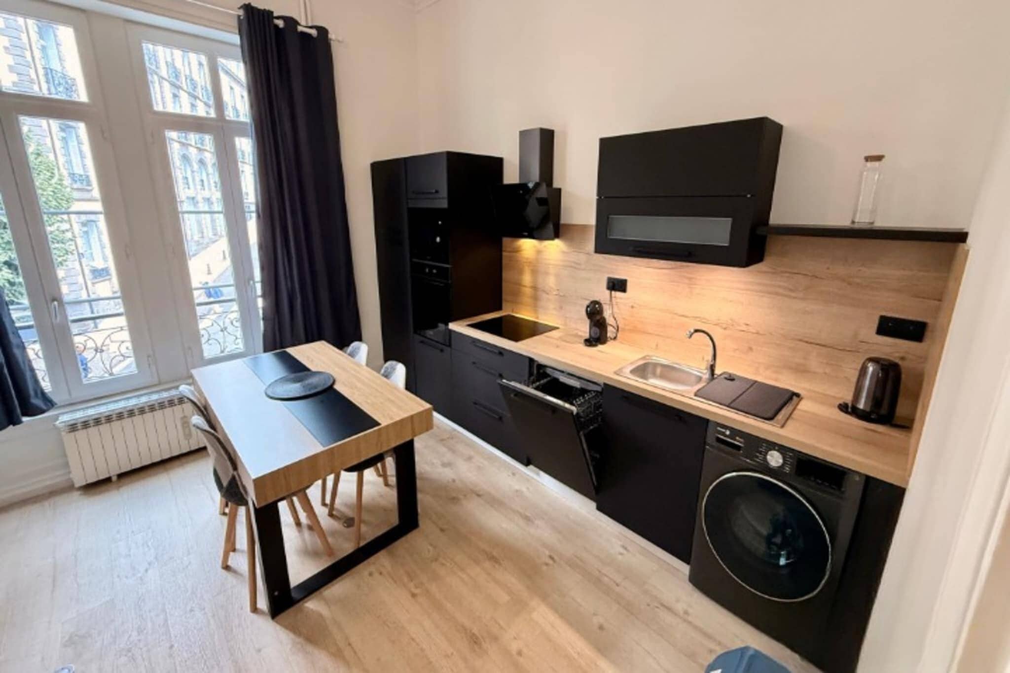 A compact kitchen with a wooden table, black cabinets, a built-in oven, and a washing machine.