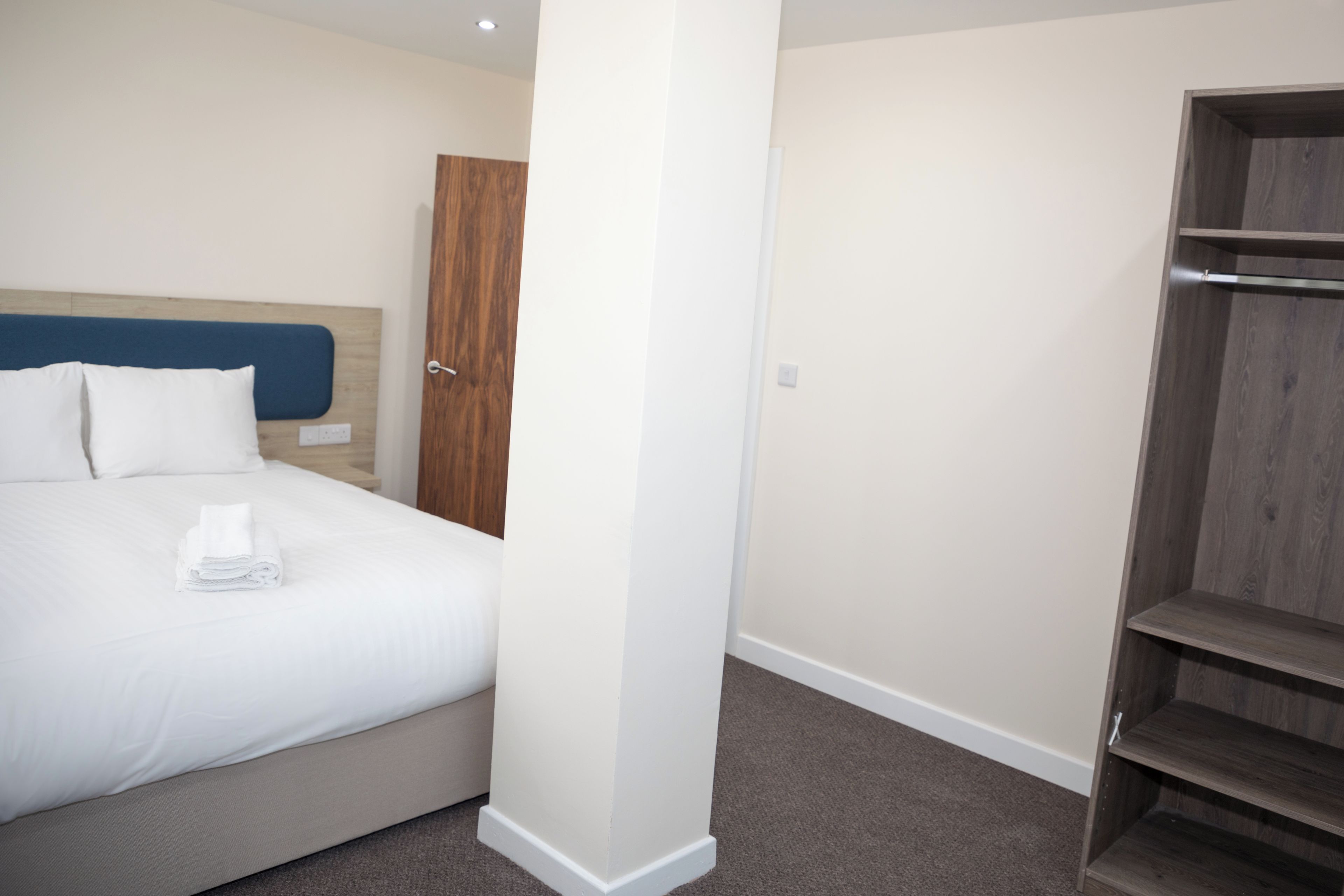 A hotel room with a bed, a wooden wardrobe, and a white pillar.