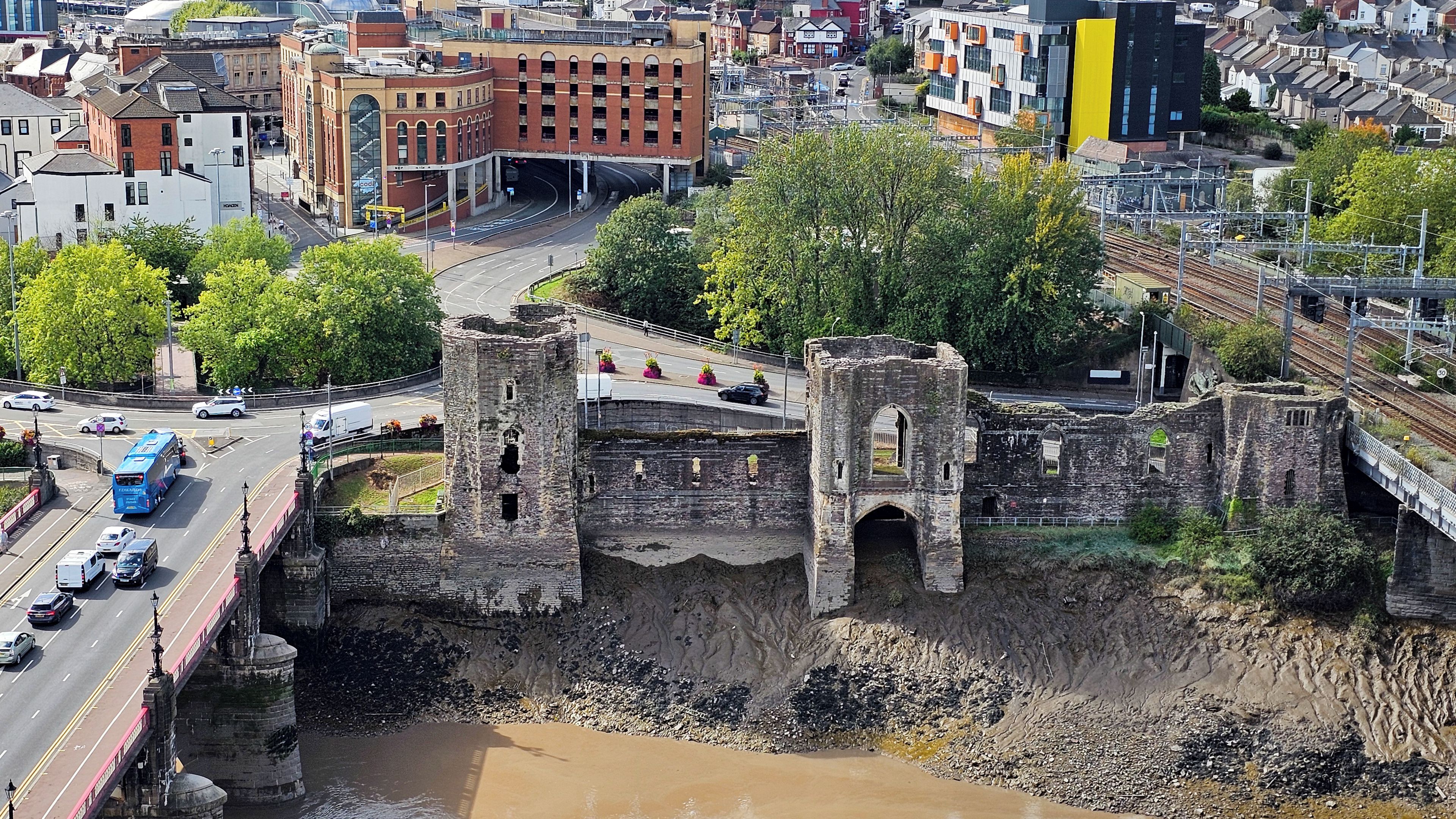 A historic stone bridge with a moat, surrounded by modern buildings and a railway track.