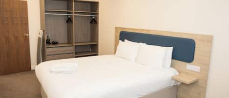 A bedroom with a bed, a wooden wardrobe, and a bedside table.