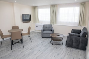 A modern living room with a grey sofa, a round coffee table, and a TV mounted on the wall. - Livin' Serviced Apartments - Newport (Newport)