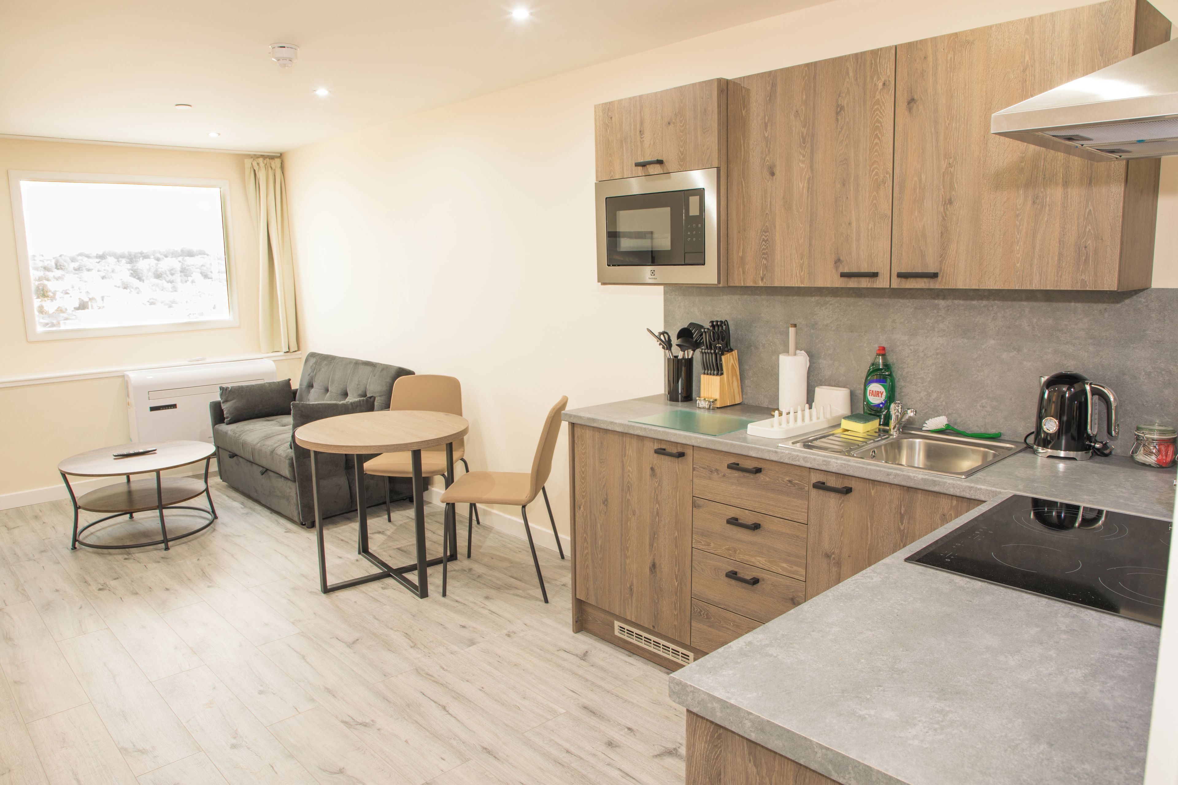 A compact kitchen with wooden cabinets, a built-in microwave, a sink, and a dining area with a table and chairs.