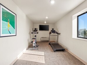 Ein kleiner, abgeschlossener Raum mit Laufband, Ergometer und einem an der Wand befestigten Flachbildfernseher.