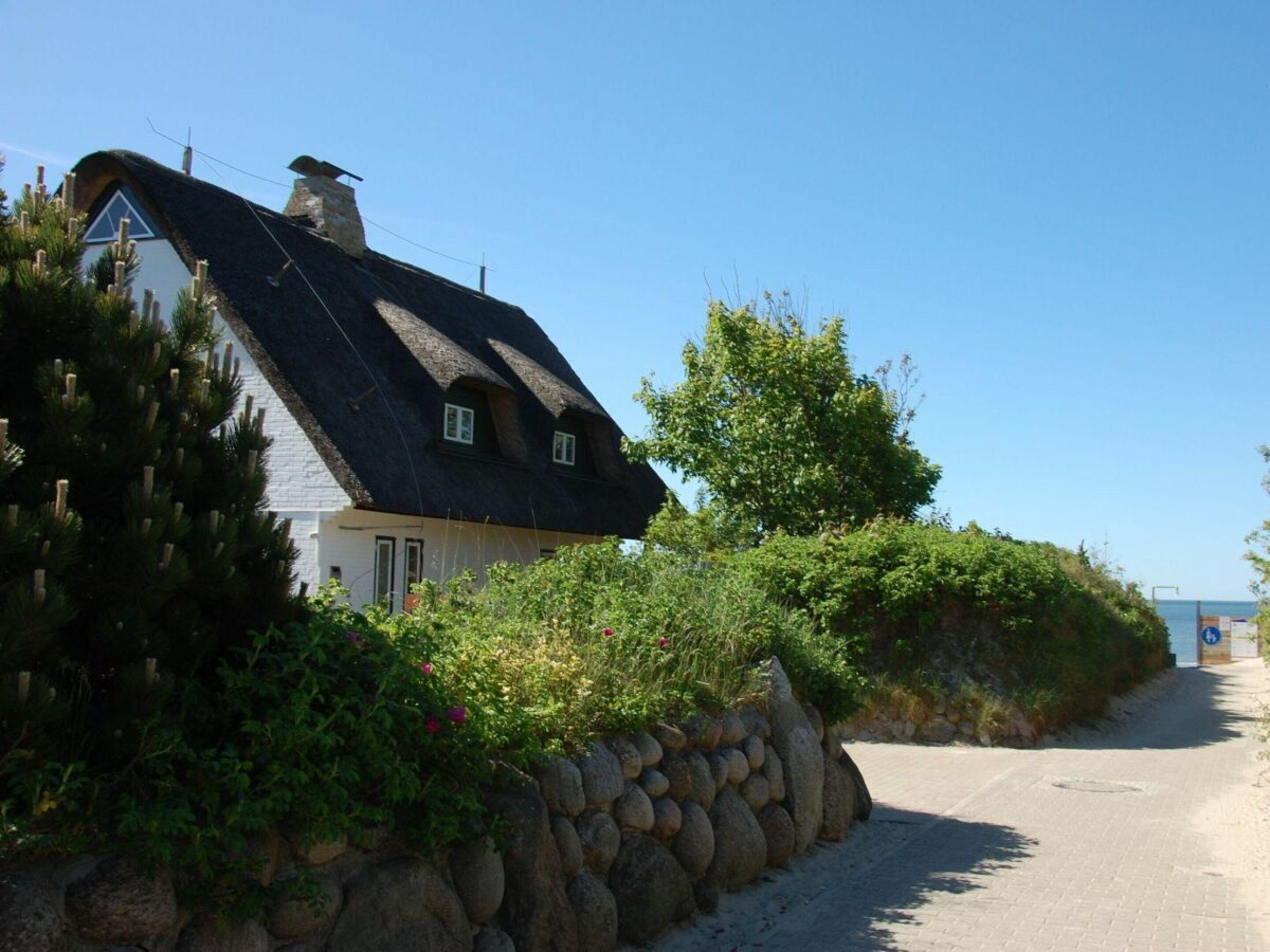 A house with a thatched roof, a stone wall, and a paved path leading to the sea.