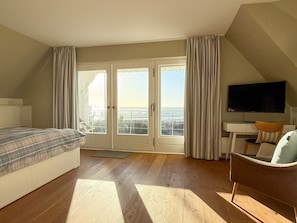A bedroom with a bed, a desk, a chair, a television, and a view of the outdoors. - Thatched House on the Beach (Wyk auf Foehr)