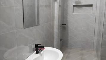 Un baño con un lavamanos blanco, un espejo y una zona de ducha.