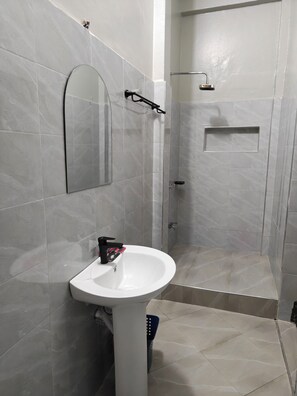 Un baño con un lavamanos blanco, un espejo y una zona de ducha.