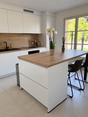 Une cuisine moderne avec des meubles blancs, un îlot central doté d’un plan de travail en bois et une fenêtre donnant sur un espace verdoyant.