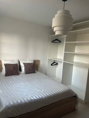 Une chambre à coucher comprenant un lit, deux oreillers, un luminaire suspendu et une armoire avec des cintres.