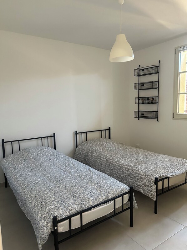 Una habitación con dos camas, una lámpara colgante y un ventanal.