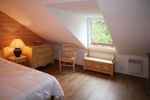 A bedroom with a sloped ceiling, a wooden dresser, a chair, a bench, and a window with a view of greenery. - 1st floor, balcony, parking, tv, ski locker, 55m², Les Orres (Les Orres)