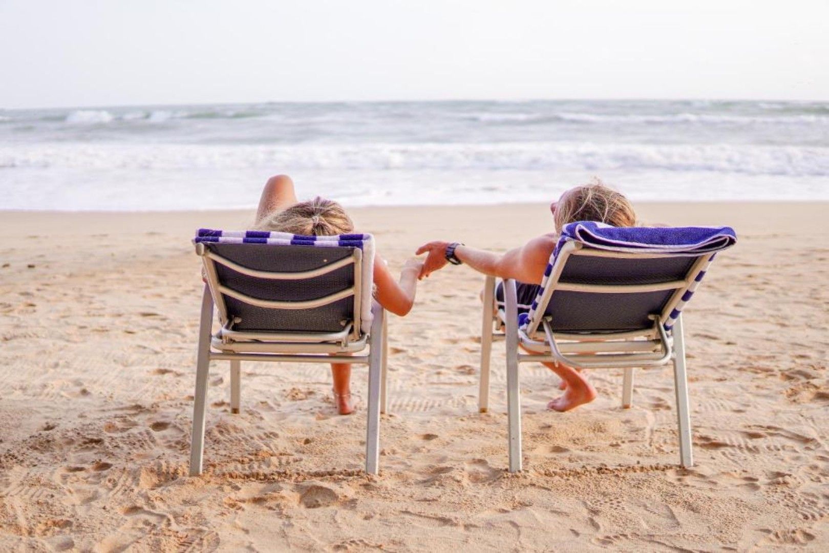 Duas cadeiras de praia viradas para o oceano, com uma praia de areia e ondas ao fundo.