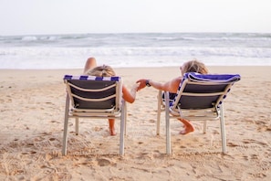Two beach chairs facing the ocean with a sandy beach and waves in the background.