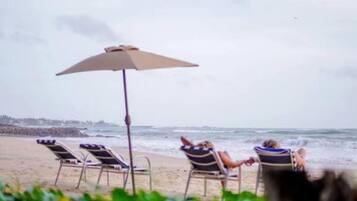 A beach scene with two lounge chairs and an umbrella, overlooking the ocean.
