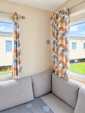 Ein Zimmer mit einem grauen Sofa, einem Fenster mit Vorhängen und Blick auf ein Haus.