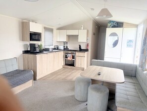 A compact living space with a kitchenette, a dining area, and seating arrangements. - Seaside Retreat 3BR Caravan New Beach Holiday Park (Dymchurch)