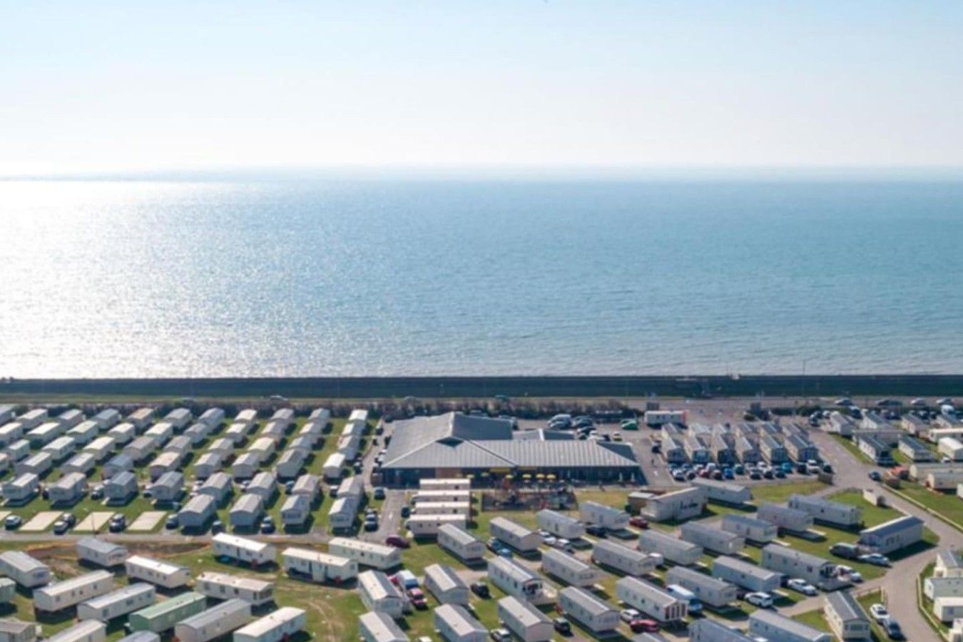 Ein Küsten-Campingpark mit mehreren Stellplätzen und einem größeren Gebäude, vermutlich ein Servicezentrum, in der Mitte.