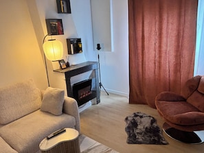 A living room with a sofa, a fireplace, a lamp, a rug, and a chair. - L'Original Duplex - Centre Ville (Liancourt)