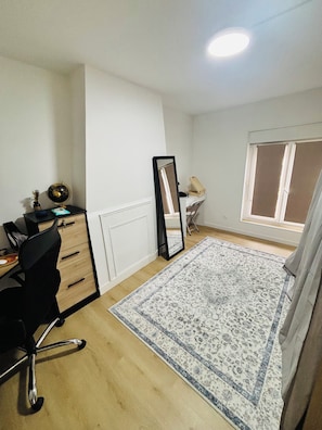 A room with a desk, chair, mirror, radiator, and a window with curtains. - L'Original Duplex - Centre Ville (Liancourt)