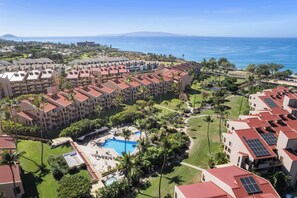 A resort with multiple buildings, a swimming pool, and a view of the ocean. - Kamaole Sands 10-302 | Resort Amenities, Across From Beach, + Great Views! (Kihei)