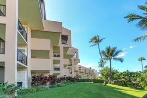 A multi-story hotel with balconies, a well-maintained lawn, and palm trees. - Kamaole Sands 10-302 | Resort Amenities, Across From Beach, + Great Views! (Kihei)