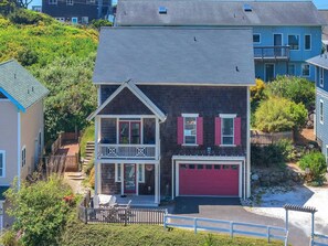 A two-story house with a red garage, a balcony, and a front porch. - Spacious Olivia Beach Home: Hot Tub, Pool, Games & Pet Friendly! Sleep 10 (Lincoln City)