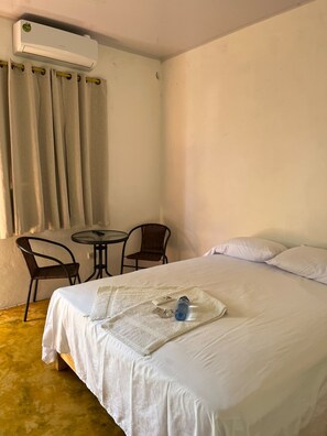 Una habitación de hotel con cama, una mesita, dos sillas, aire acondicionado y una ventana con cortinas.