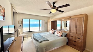 Ein Schlafzimmer mit Bett, Deckenventilator, Fernseher und Blick auf den Strand.