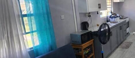 A living room with a sofa, a television, and a kitchen area with cabinets and a microwave.