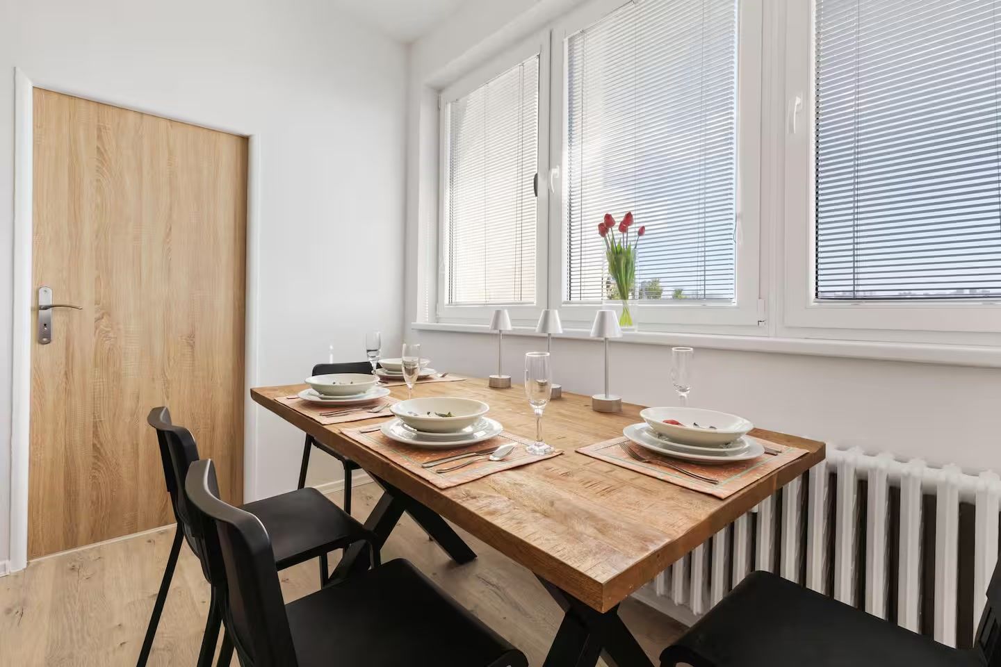 Een eetgedeelte met een houten tafel voor vier personen, witte borden en glazen.