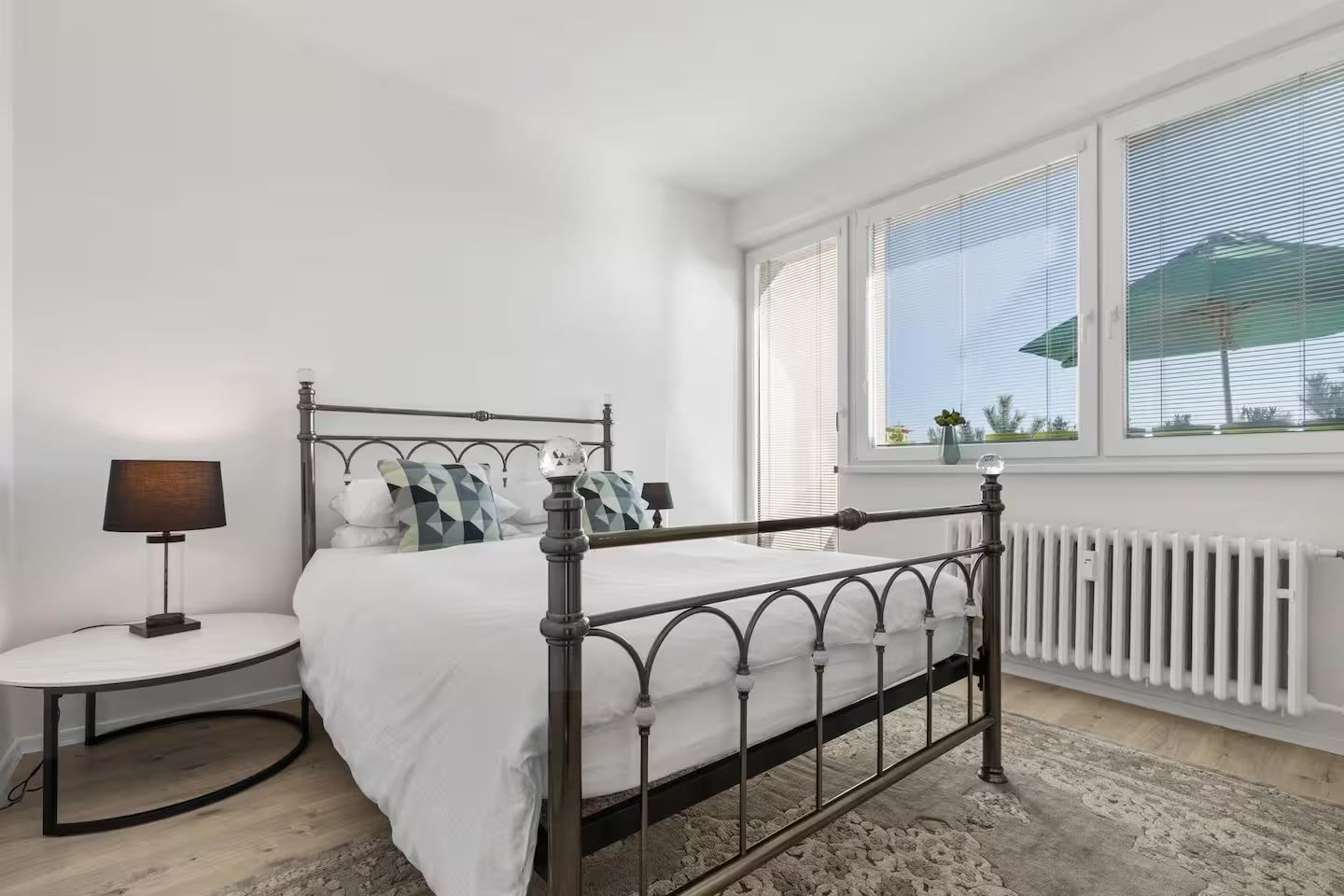 Een slaapkamer met een bed met metalen frame, witte beddengoed, een bedlampje en een raam met zonwering.