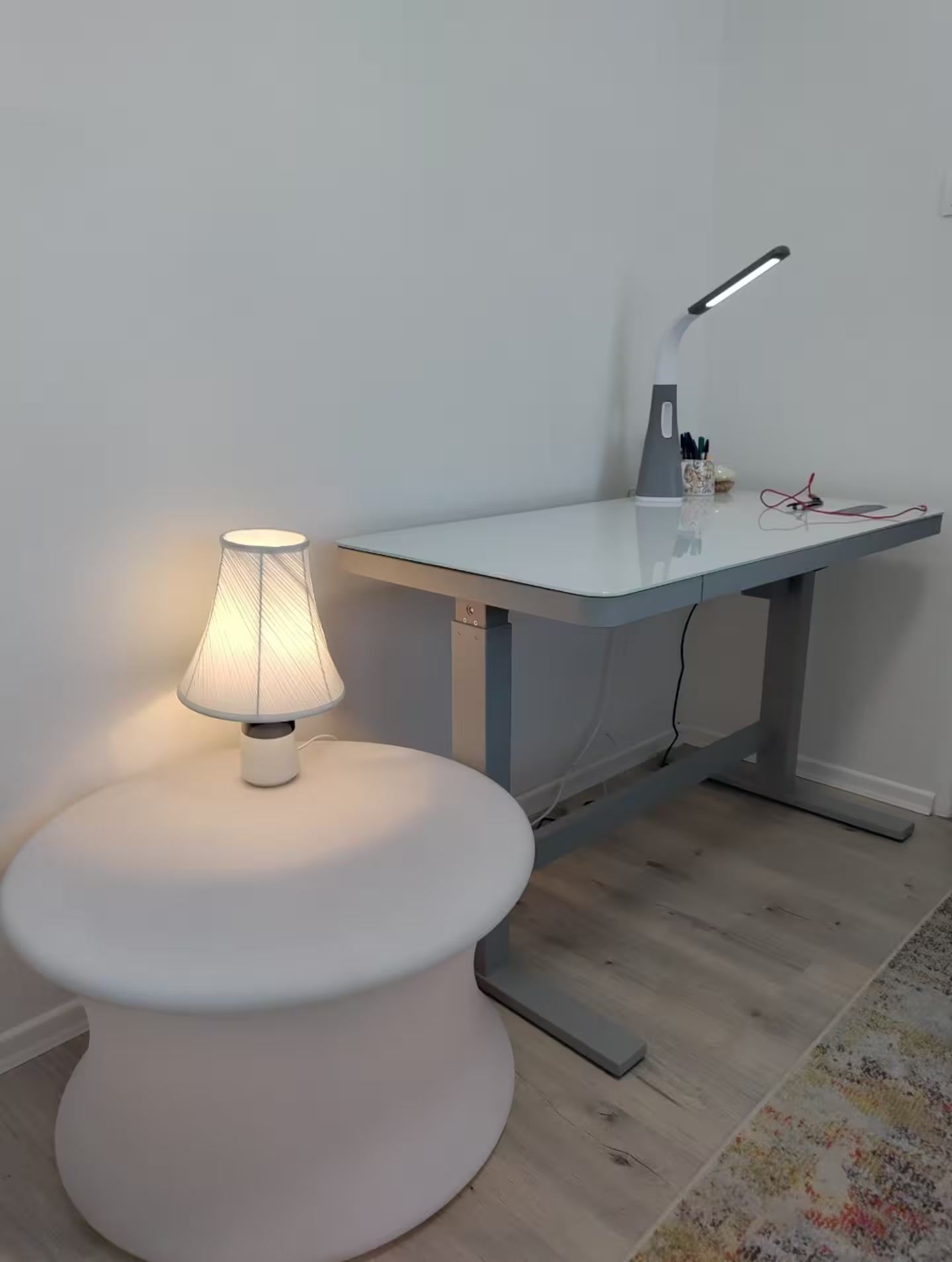 Ein moderner Arbeitsplatz mit einem runden weißen Tisch, einem Schreibtisch mit einer Lampe und einem kleinen Teppich.