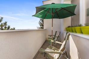 A small balcony with a green umbrella, a chair, and potted plants.