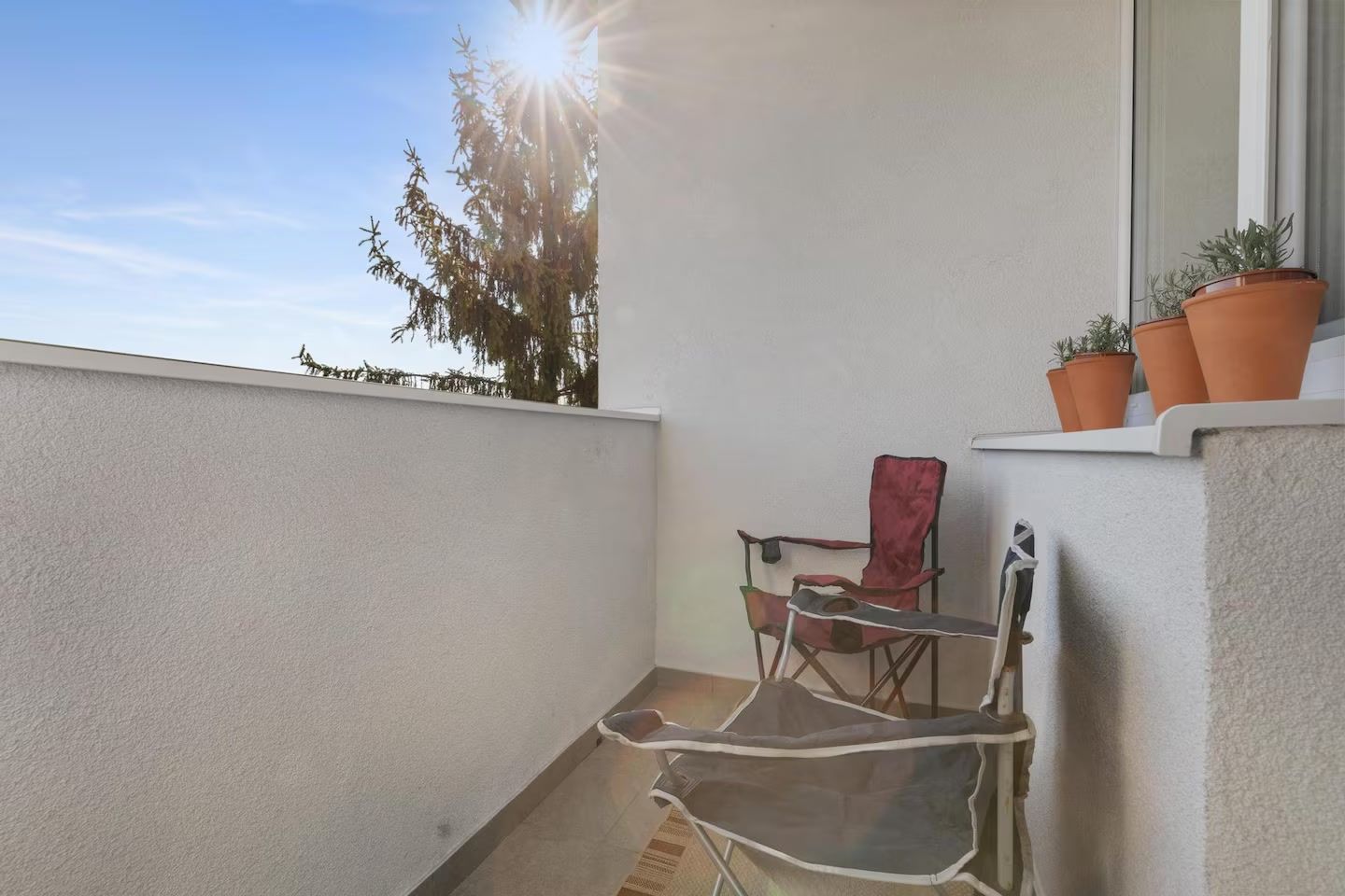 Ein Balkon mit einem Stuhl, einem kleinen Tisch und Blumentöpfen.